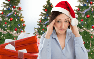 A fair-skinned woman with brown hair has a santa hat on and looks tense. There are several red packages behind her and a few decorated Christmas trees.