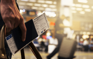 A Deaf traveler holding a passport and boarding pass is inside a busy airport.